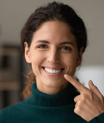 Woman in green turtle neck pointing to her perfect smile