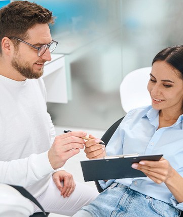 Dentist handing pen to patient in dental chair to sign financial forms
